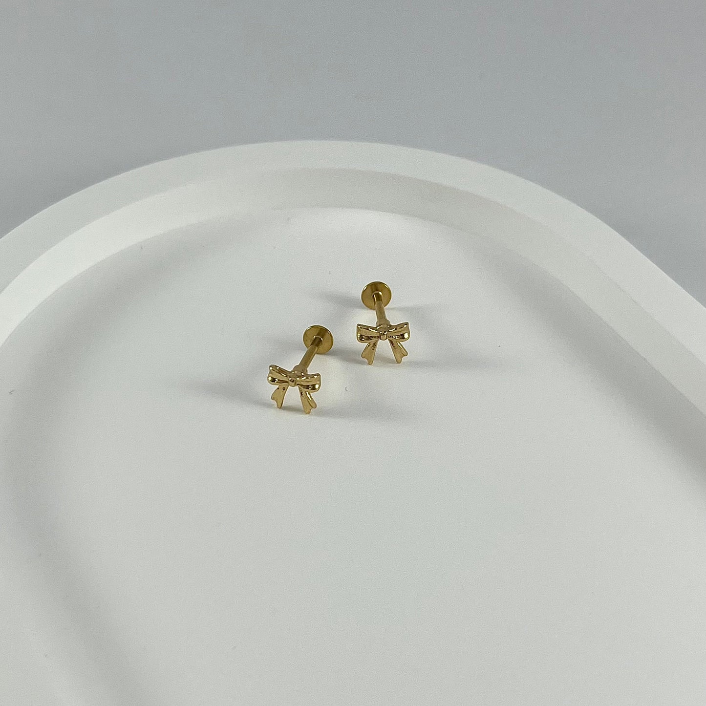 Gold bow-shaped flatback earrings on a white surface.