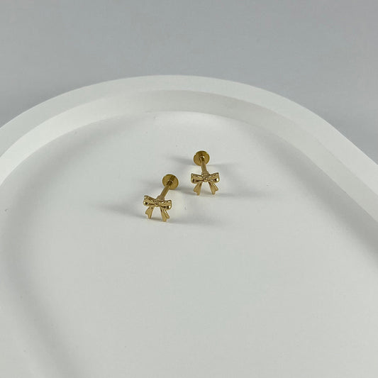Gold bow-shaped flatback earrings on a white surface.