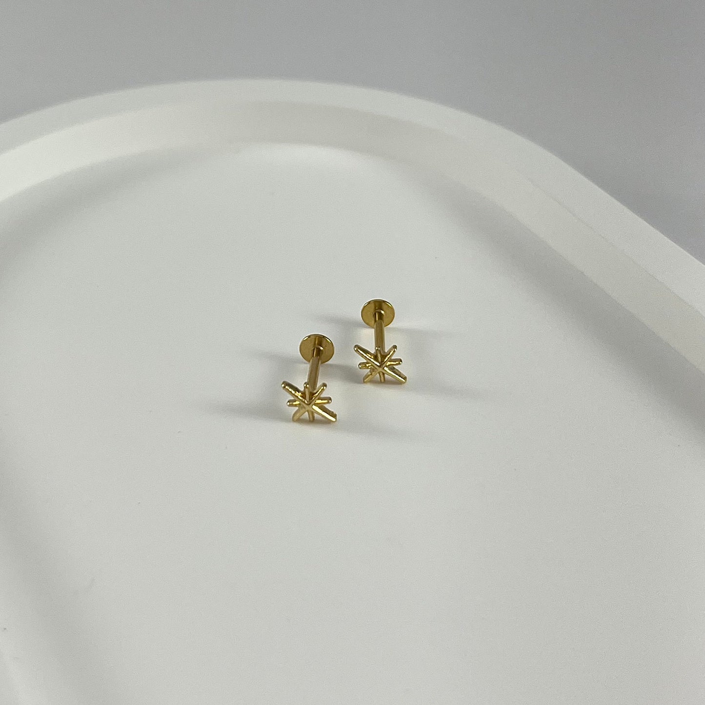Gold star-shaped flatback earrings on a white plate.