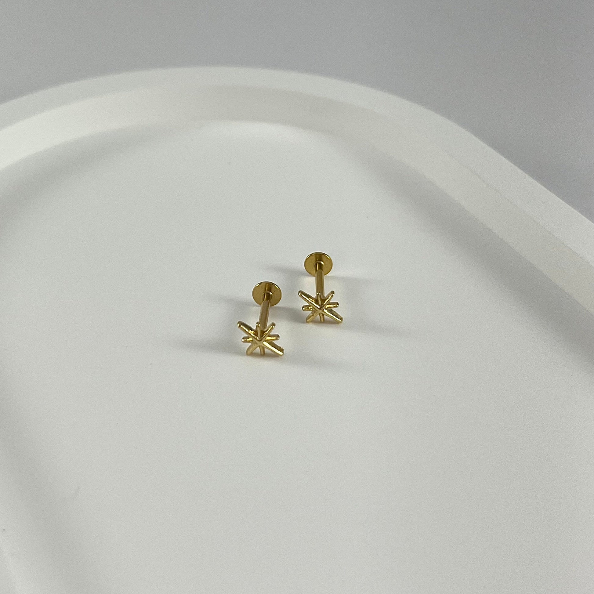 Gold star-shaped flatback earrings on a white plate.